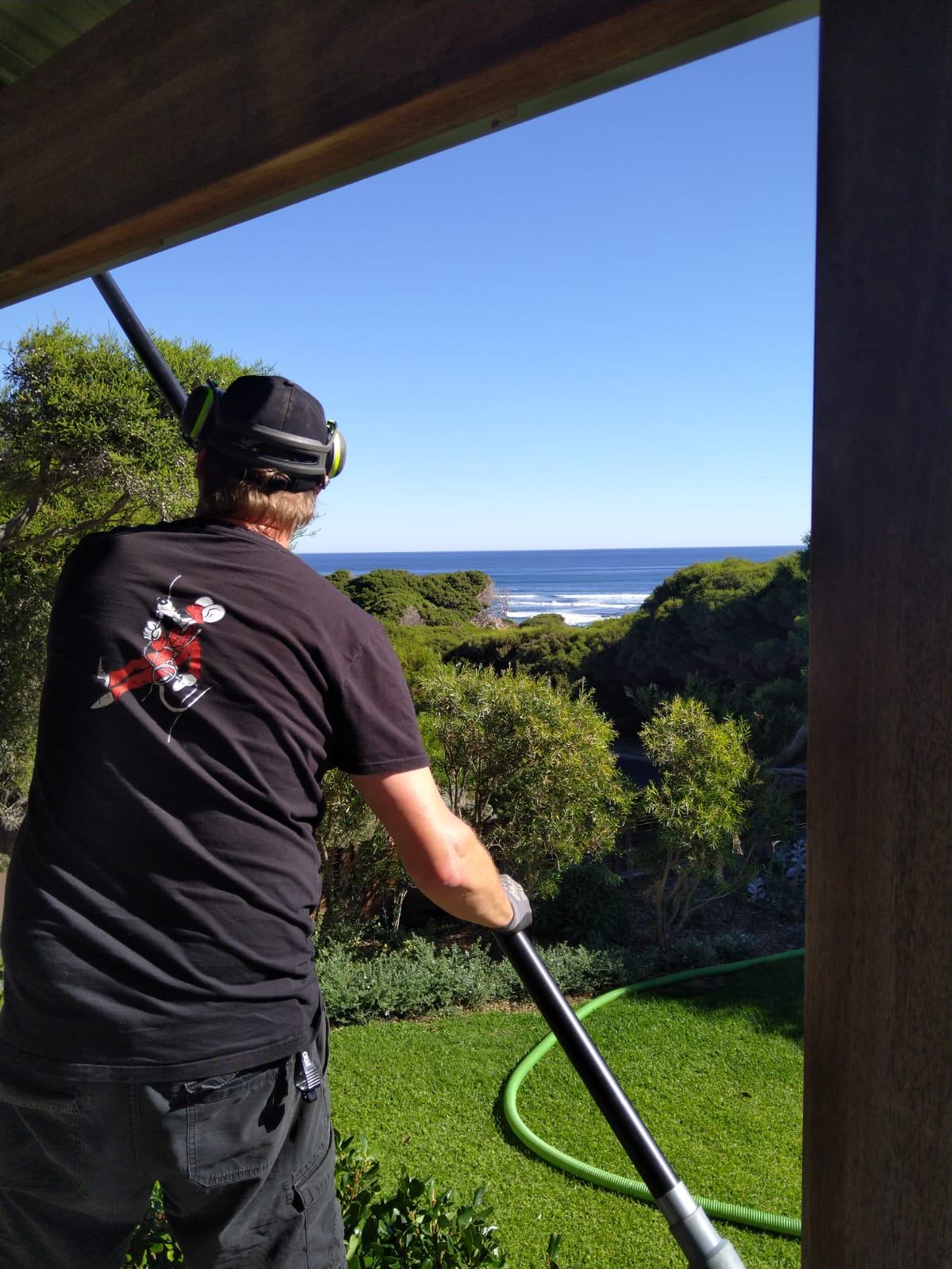 Roof Rats worker with the rat logo on his shirt using a vacuum pole at a coastal property