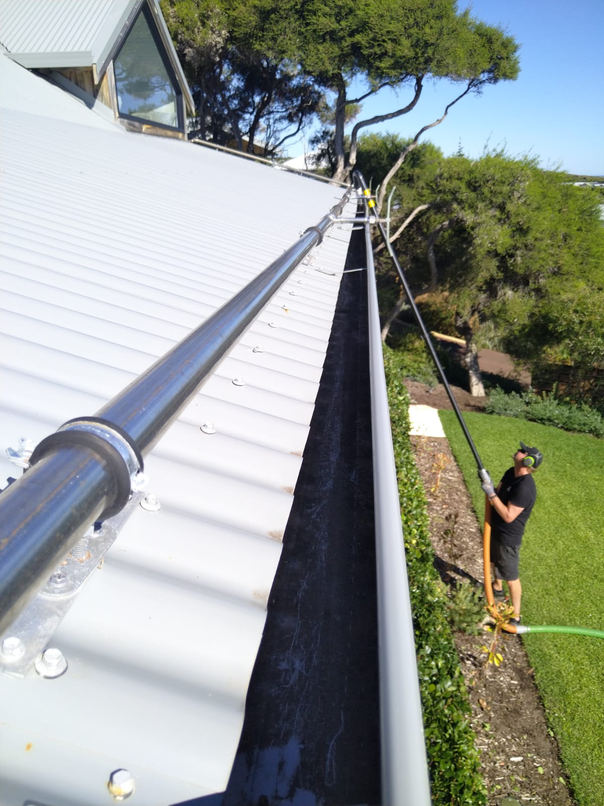 Long clean gutter run on a white roof being vacuumed from the ground with a pole